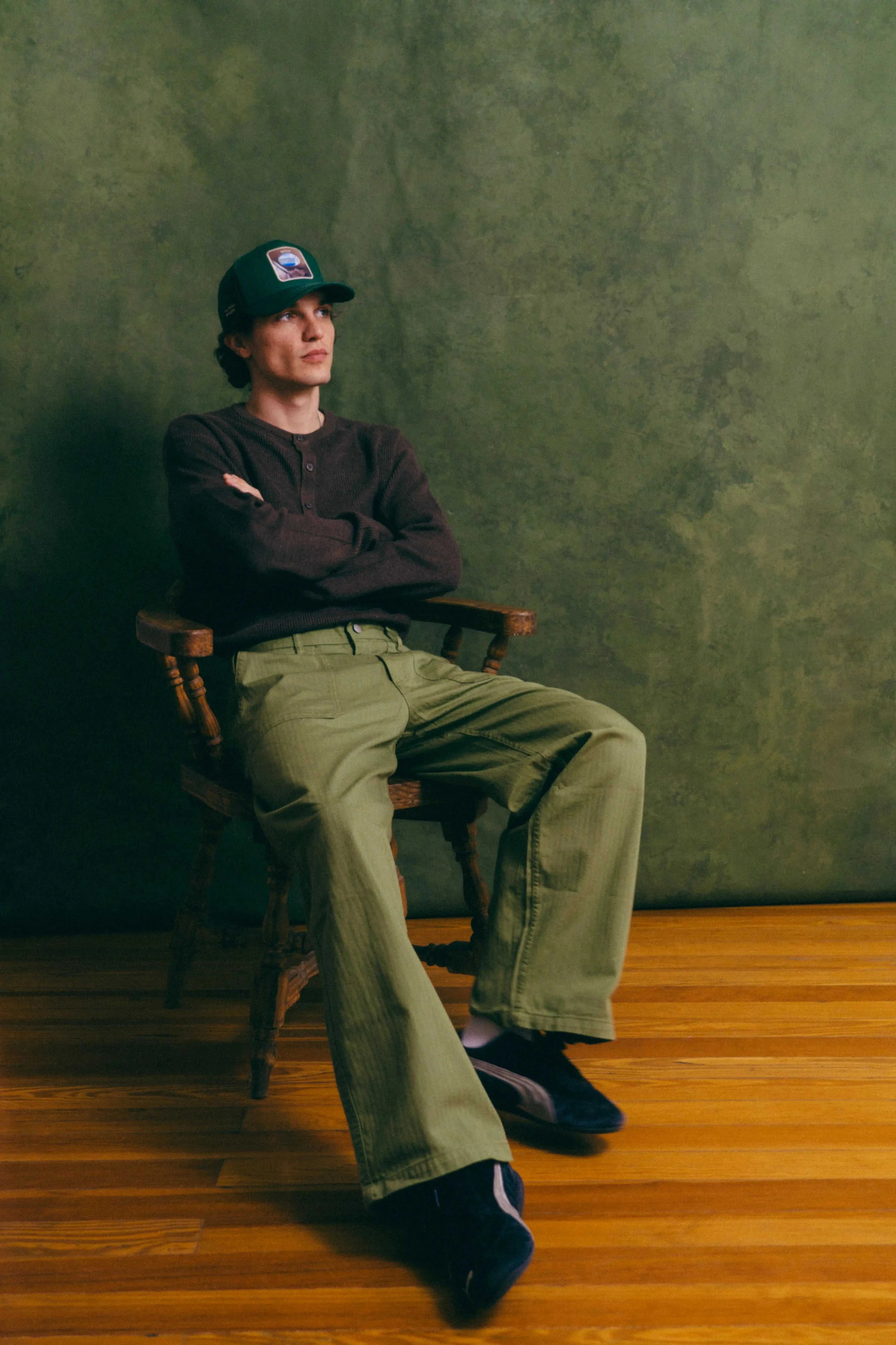 Man wearing Ovals Baseball Cap sitting on wooden chair with green background