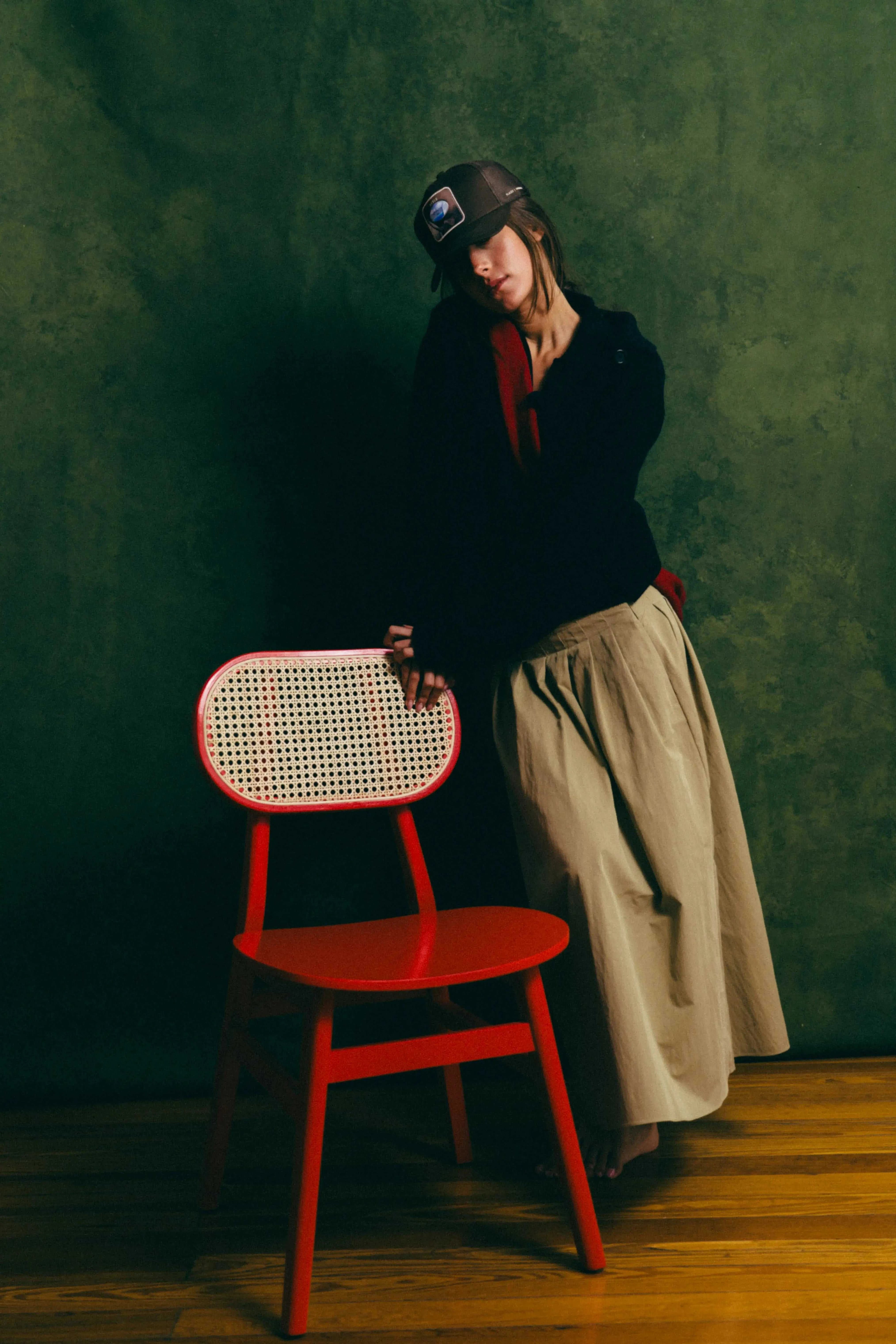 woman wearing Ovals Mesh-Back Trucker Hat standing next to red chair with green background