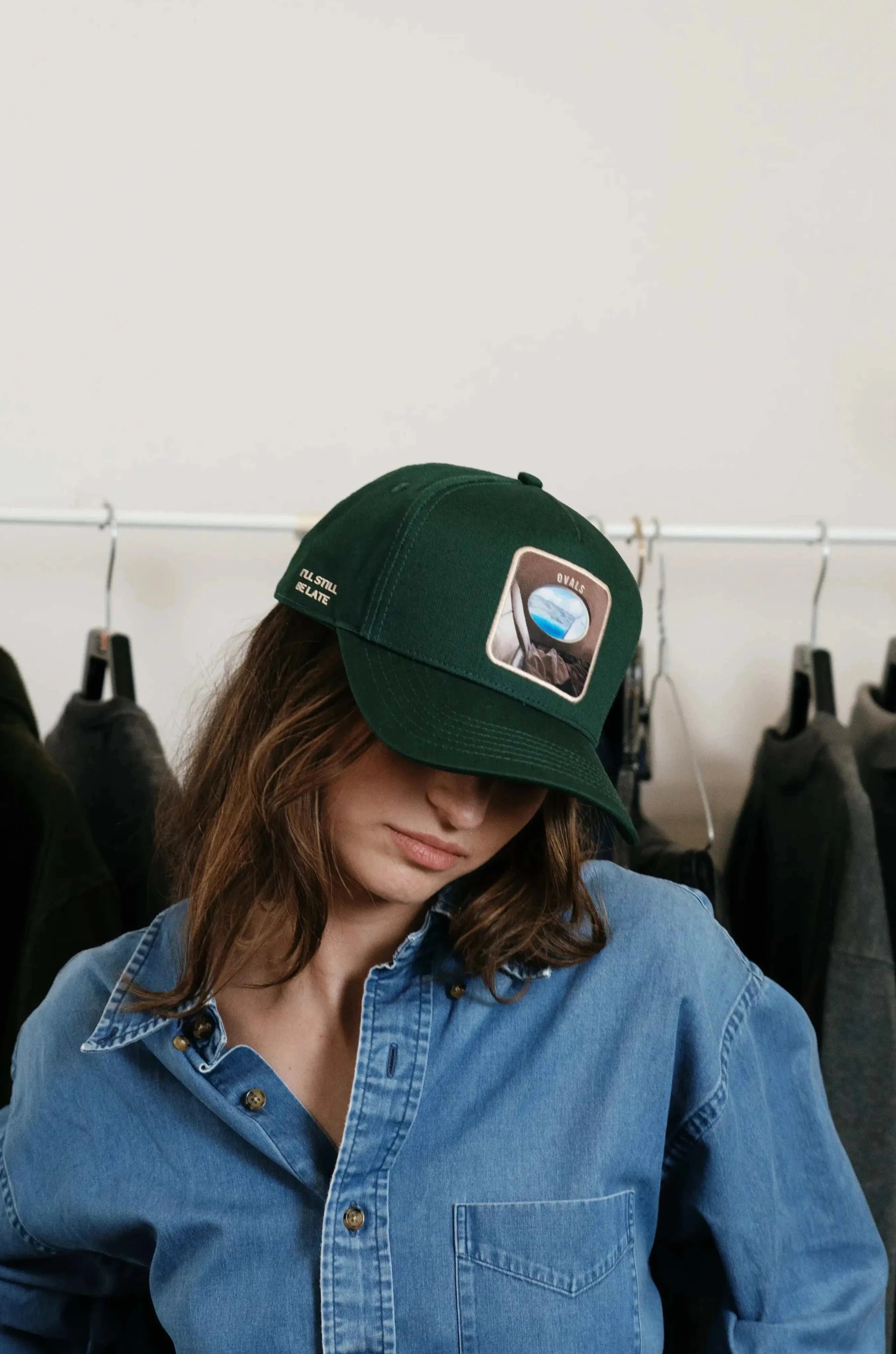 Woman wearing forest green Ovals Baseball Cap with embroidered patch and denim shirt indoors