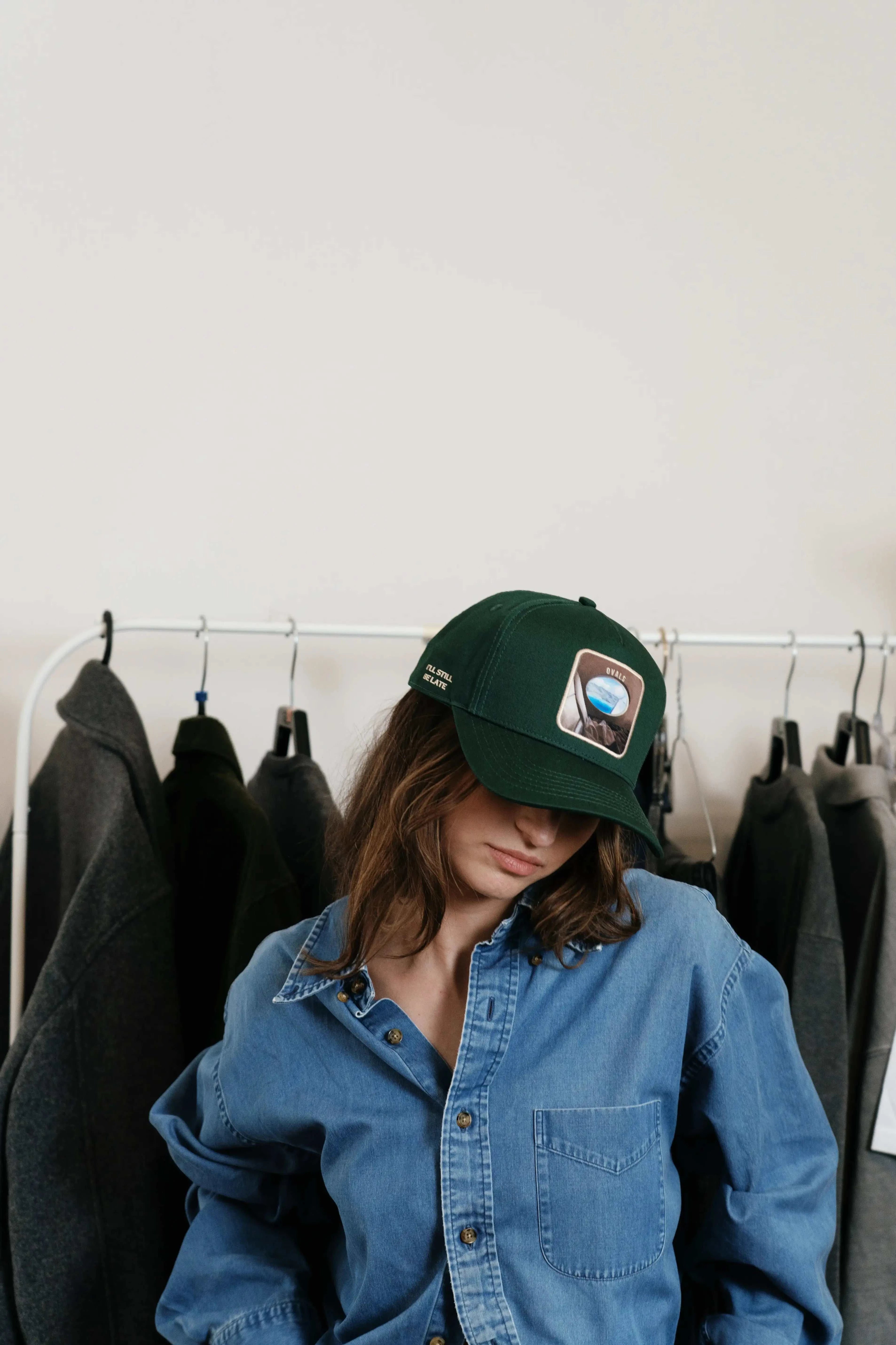 Woman wearing forest green Ovals Baseball Cap with embroidered patch and denim shirt indoors