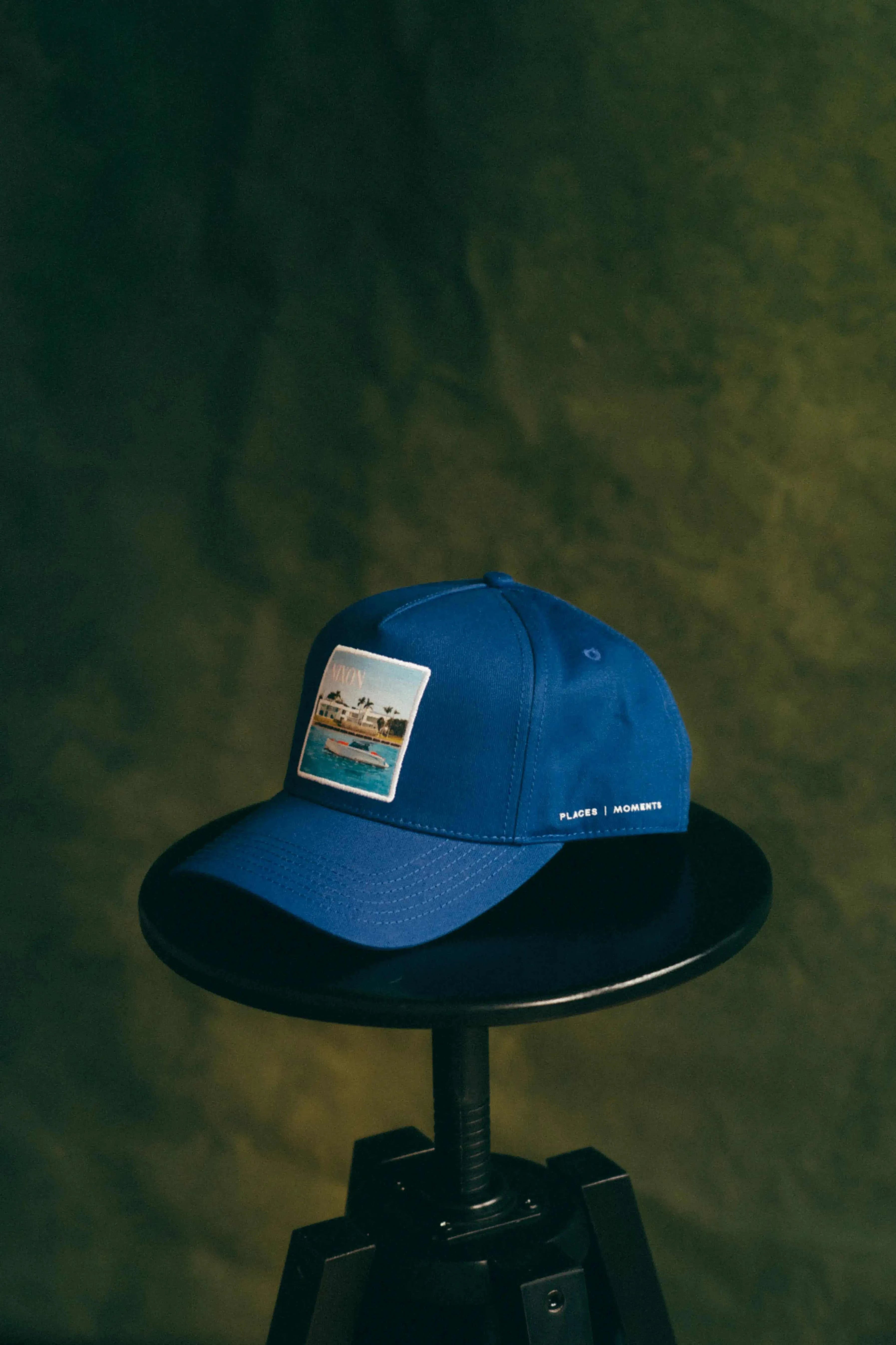 Blue Nixon Baseball Cap with curved brim and Places | Moments patch on black stool
